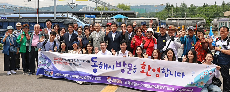 기차역 앞에서 참가자들과 동해시 방문을 환영합니다란 플랫카드를 배경으로 단체사진